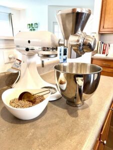 Stand mixer with a grain mill attachment and a bowl of dried sprouted wheat berries.
